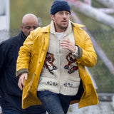 Ryan Gosling wearing the Yellow Coat over a white wolf-patterned knit cardigan and blue beanie.